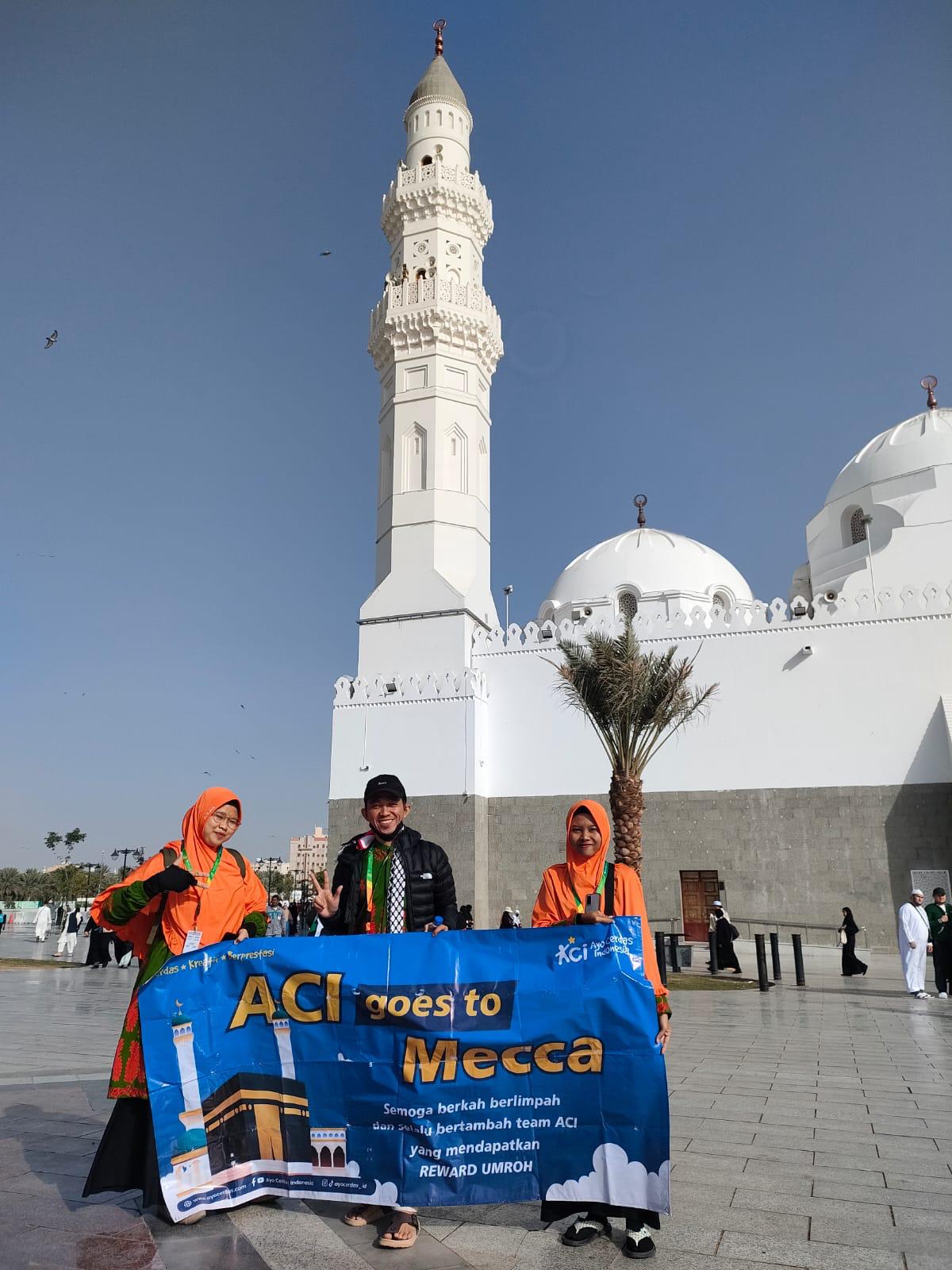 Anggota tim ACI membawa banner Reward Umroh di depan bangunan masjid
